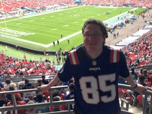 Fanclub-Mitglied im Patriots-Jersey im Stadion, im Hintergrund das Spielfeld