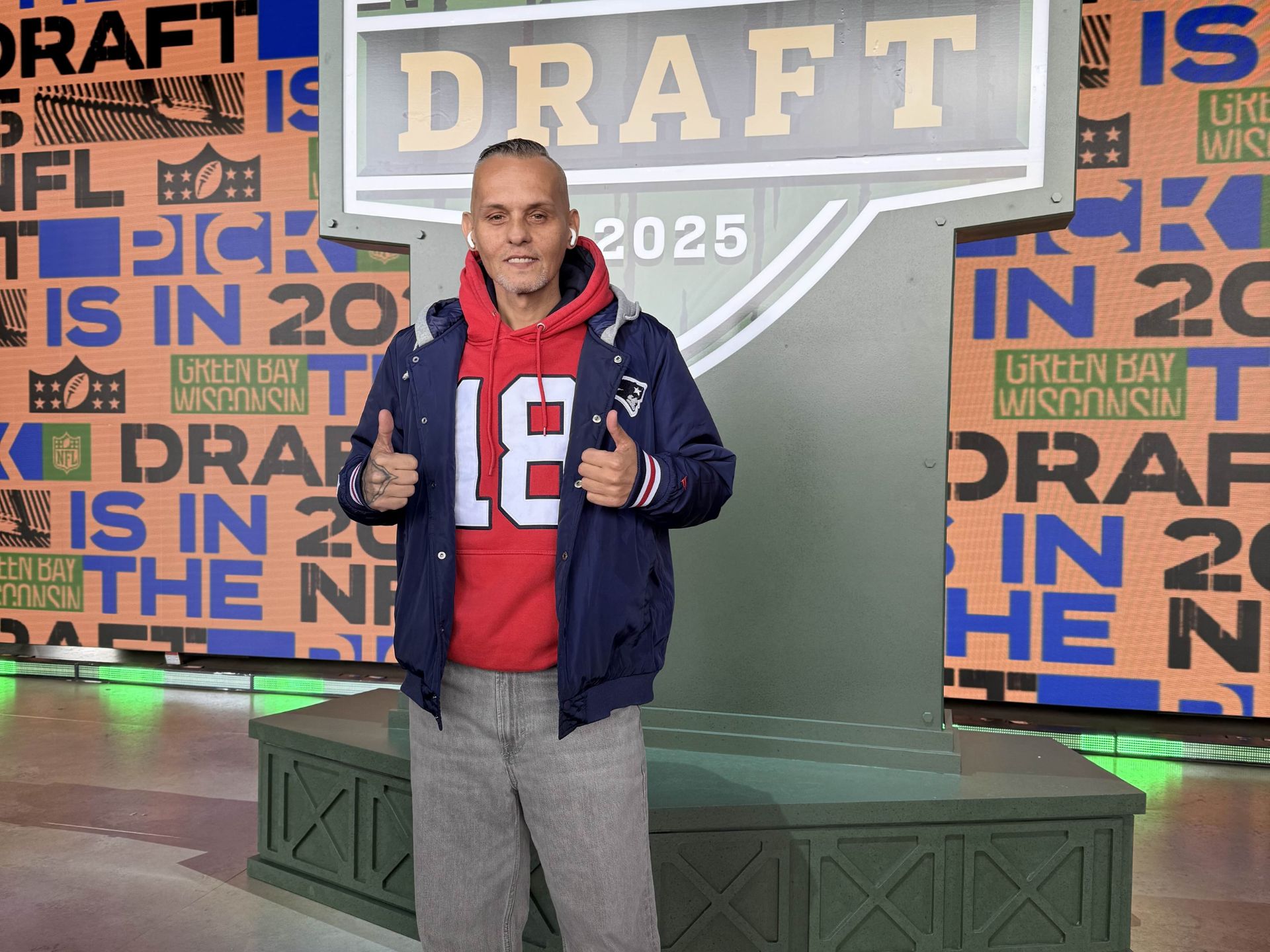 IFOTY Dennis im Patriots Jersey posiert vor dem NFL Draft Logo