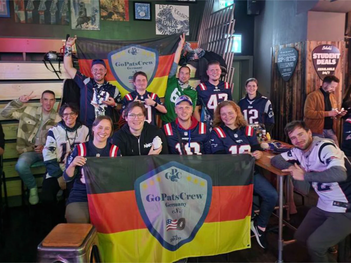 Eine Gruppe von GPC-Mitgliedern in einem Gruppenbild. Die Fanclub-Fahne ist einmal vorne und einmal hinten gespannt. Sie sitzen in einem Pub in London.
