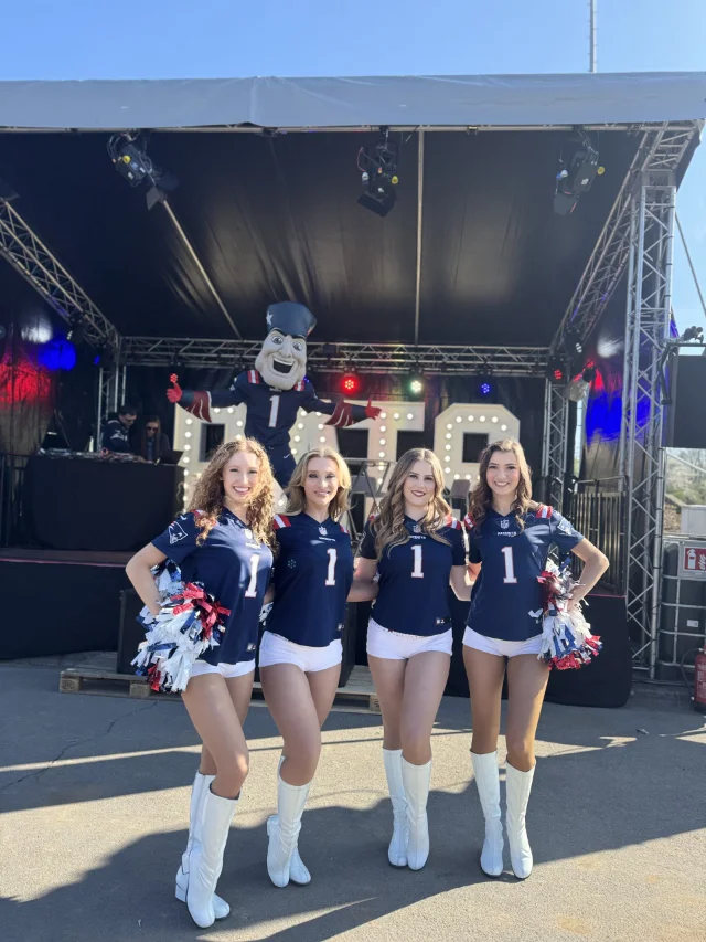 Vier Cheerleader posieren für die Kamera, Pat Patriot steht im Hintergrund.