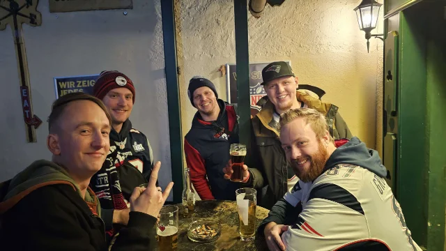 Fünf Mitglieder stehen mit Bier und anderen Getränken um einen Stehtisch.