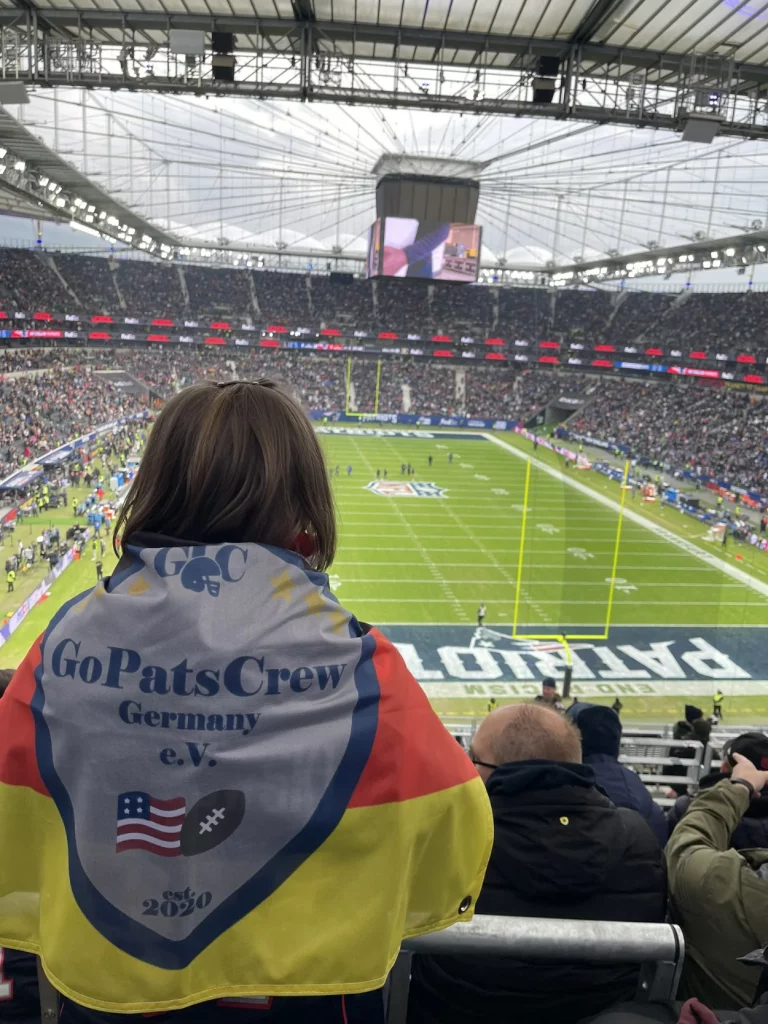 Ein Mitglied, mit einer Patriots-Fahne auf den Schultern, steht auf den R&auml;ngen im Waldstation. Das Spielfeld im Hintergrund