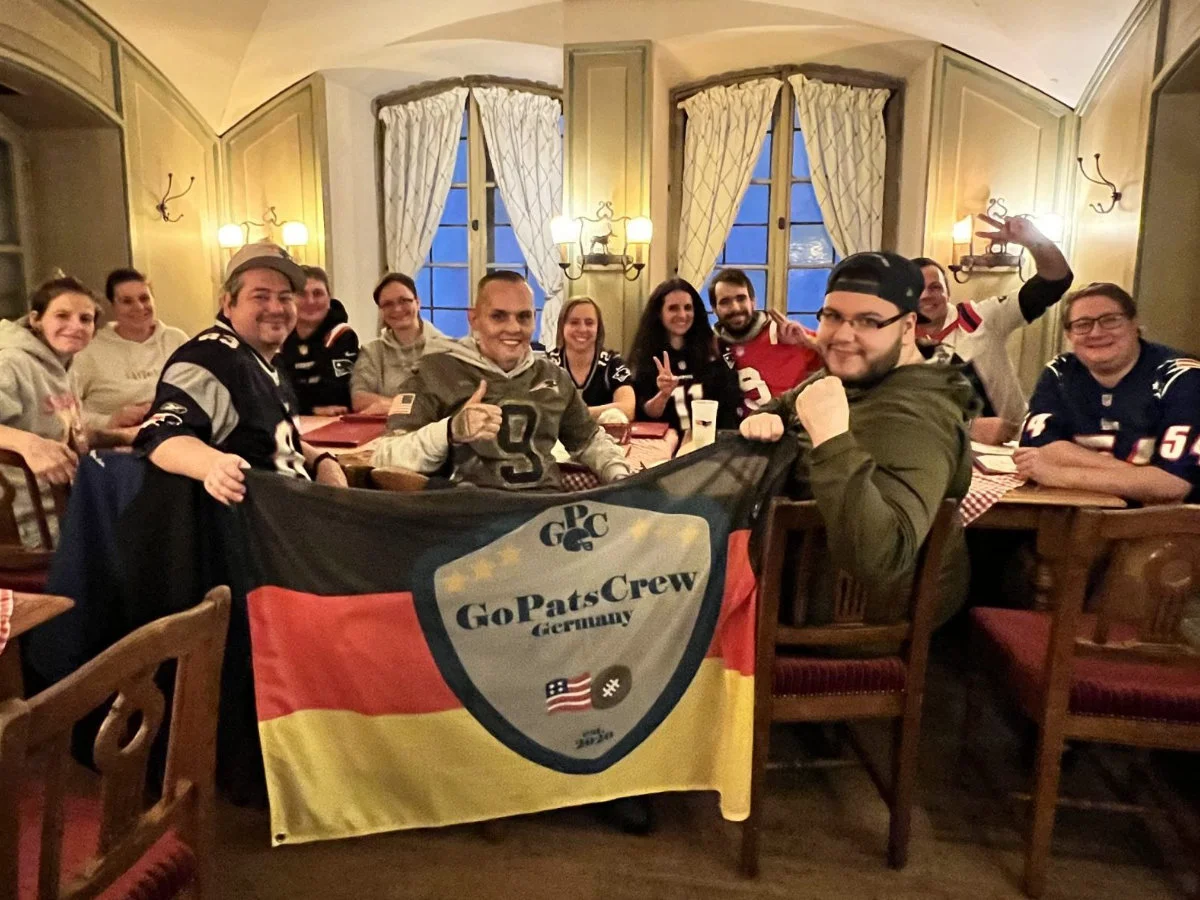 Mitglieder der GoPatsCrew sitzen an einem Tisch im Ratskeller in München und halten eine Fanclub-Fahne
