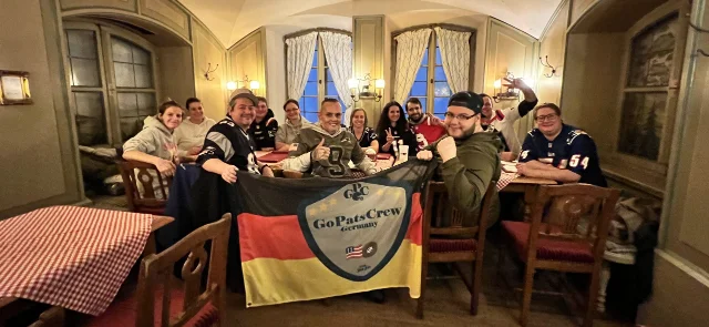 Mitglieder der GoPatsCrew sitzen an einem Tisch im Ratskeller in München und halten eine Fanclub-Fahne