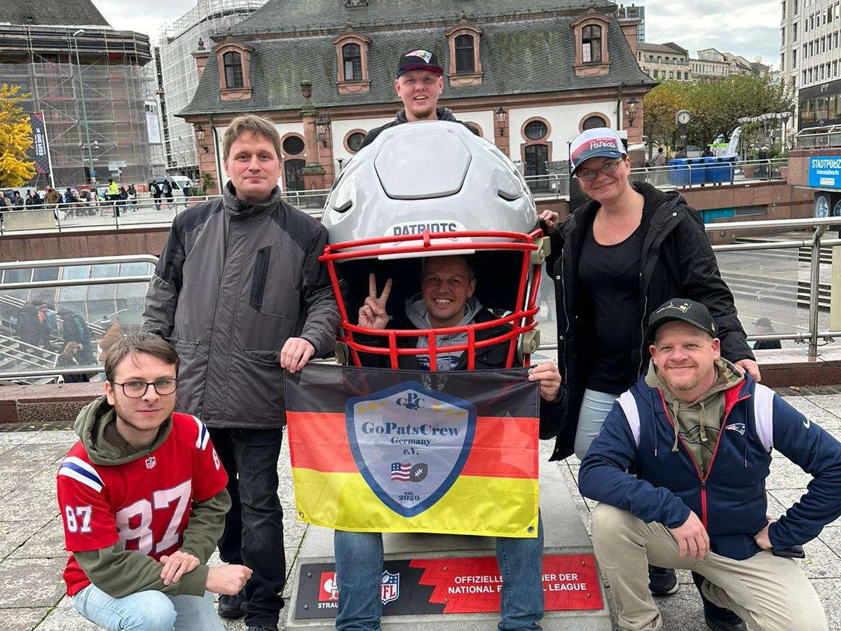 Sechs Mitglieder der GoPatsCrew stehen um einen großen Footballhelm in Frankfurt am Main und halten die Fanclub-Fahne hoch.