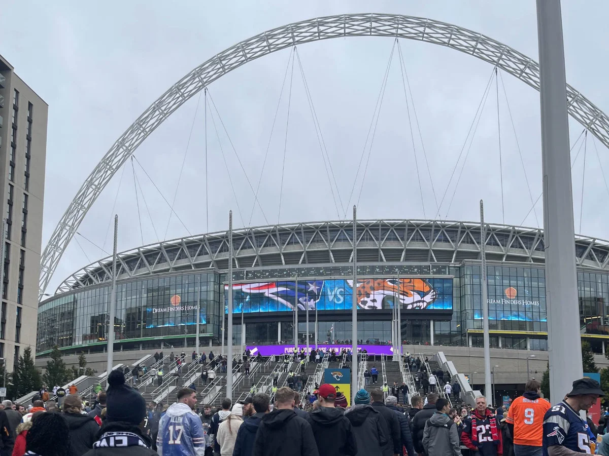 Eine Menschenmenge geht Richtung Wembley-Stadion in London. Auf dem Display ist die Spielbegegnung zu sehen (Patriots gegen Jaguars).
